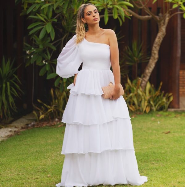 VESTIDO LONGO BRANCO DE UM OMBRO SÓ E MANGA LONGA E SAIA EM BABADOS FLUIDOS.